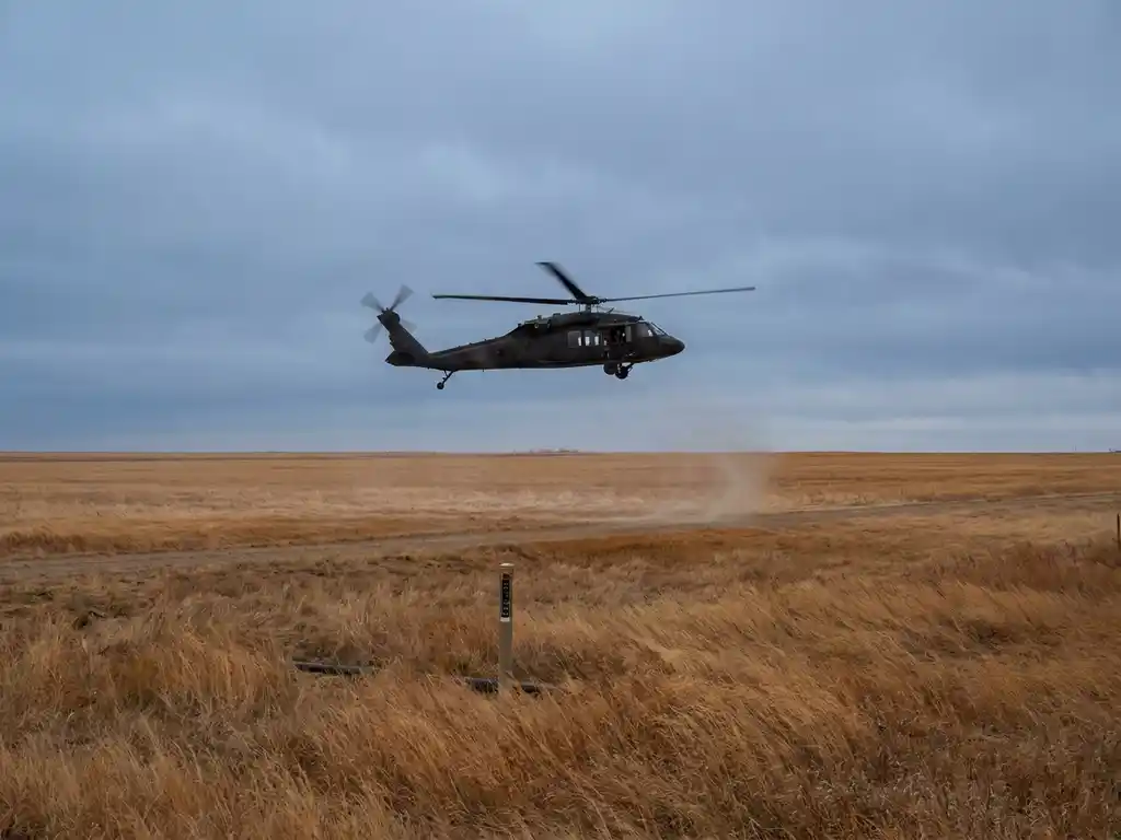 Helicopter flying low over amber rural fields scanning for methane leaks in buried pipeline infrastructure beneath wind-bent grass.
