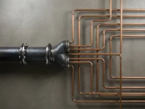 Steel transmission pipe branching into smaller copper distribution lines on concrete, overhead view showing industrial pipeline network.