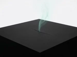 Pale teal gas rising from a hairline crack in a matte black geometric surface against clean negative space.