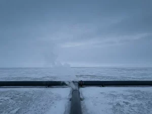 Pale gas wisps rising from an underground pipeline cross-section into arctic air, charcoal and steel blue minimalist landscape.